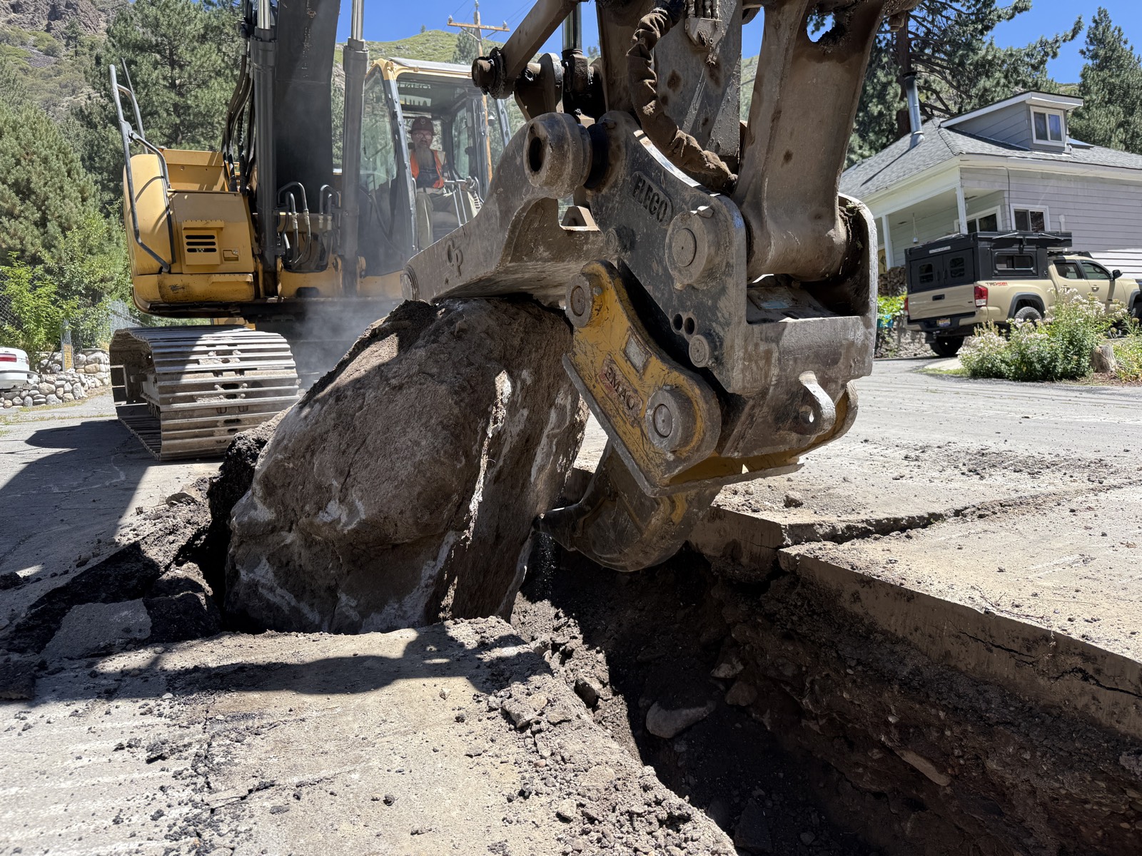 Excavator pulling a large boulder from a utility trench on a Truckee mountain jobsite