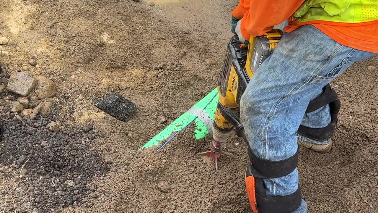 Excavation worker using a DeWalt SDS max rotary hammer to break through compacted ground near utility markings — compaction testing field guide by Errol Kerr